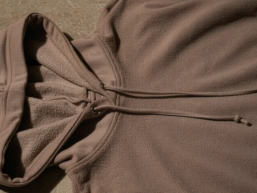 Tissu polaire brossé avec cordon de serrage sur la capuche et œillets métalliques sur un sweat à capuche plié.