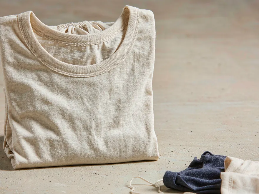 Muestras de jersey de algodón de calibre fino y una camiseta doblada que muestra el cuello acanalado y la textura del tejido.