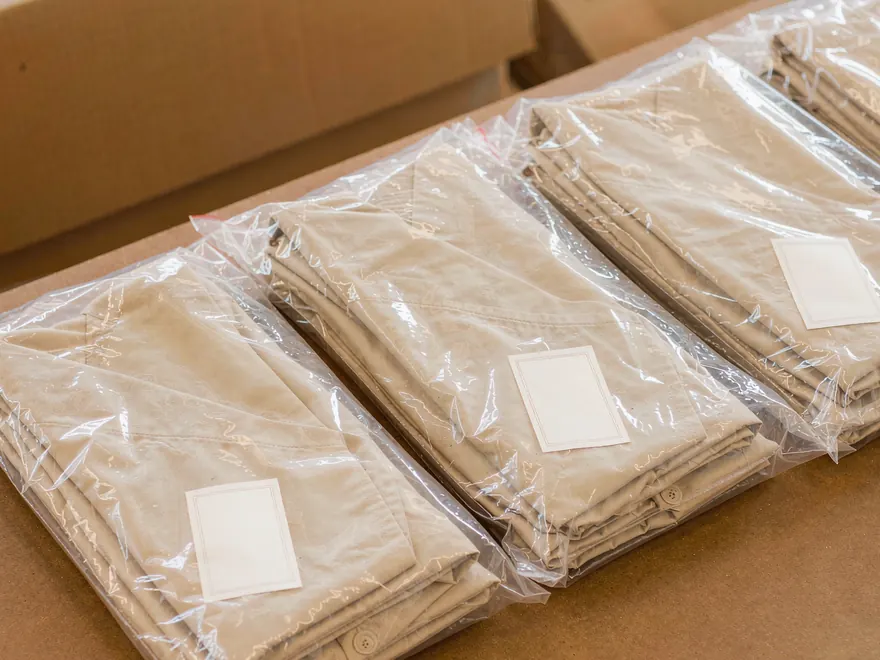Gefaltete Kleidungsstücke, verpackt in Polybeuteln in einem Versandkarton.
