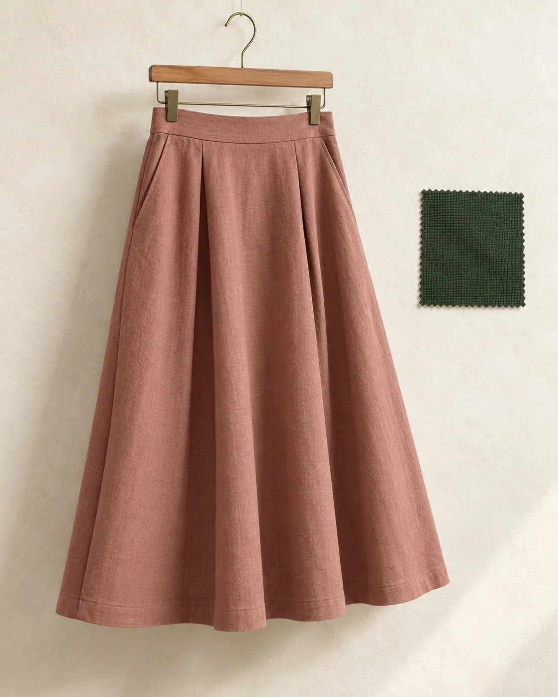 Unbranded dusty rose midi skirt with front pleats on a clip hanger, with a woven fabric swatch beside it.