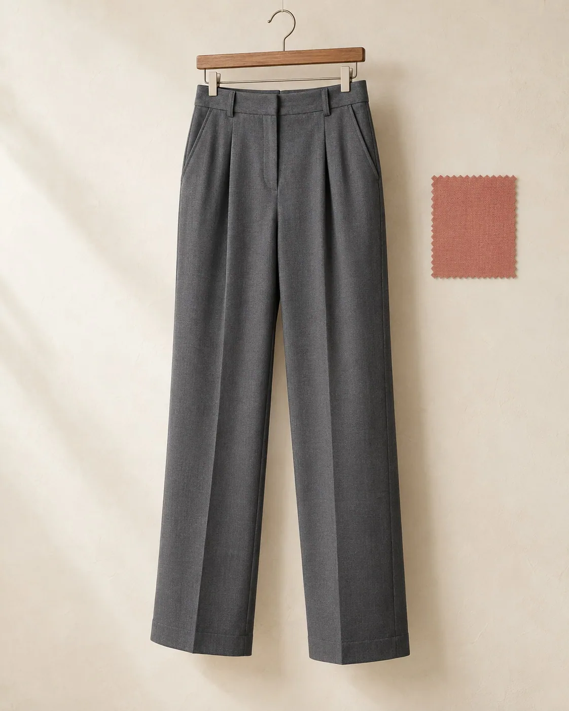 Unbranded grey pleated wide-leg trousers on a clip hanger, with a woven fabric swatch beside them.